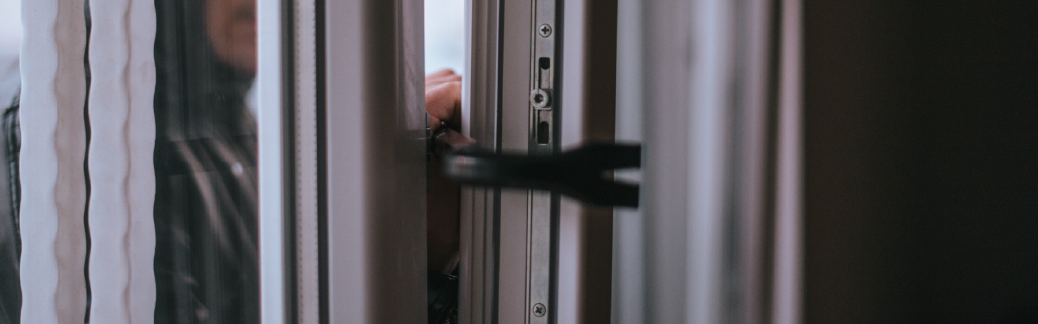 Burglar dressed in dark colored clothing attempting to break into a home using a crowbar